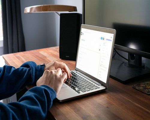 Hands resting on a wooden desk next to a laptop